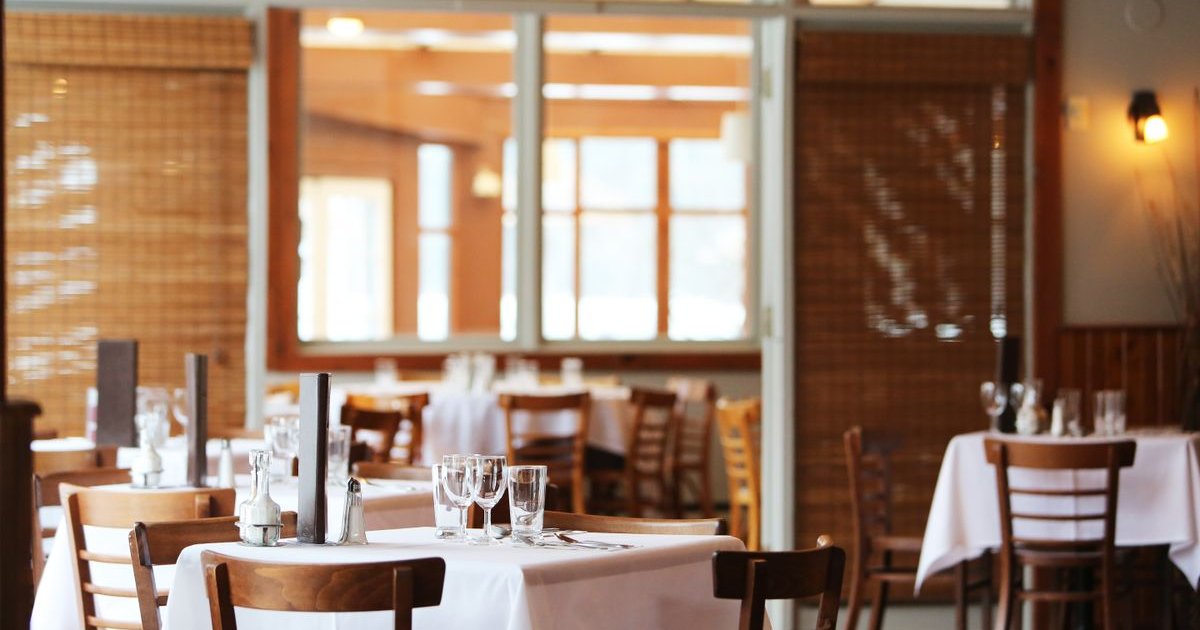 Inside of a warm, inviting restaurant with set tables and natural lighting